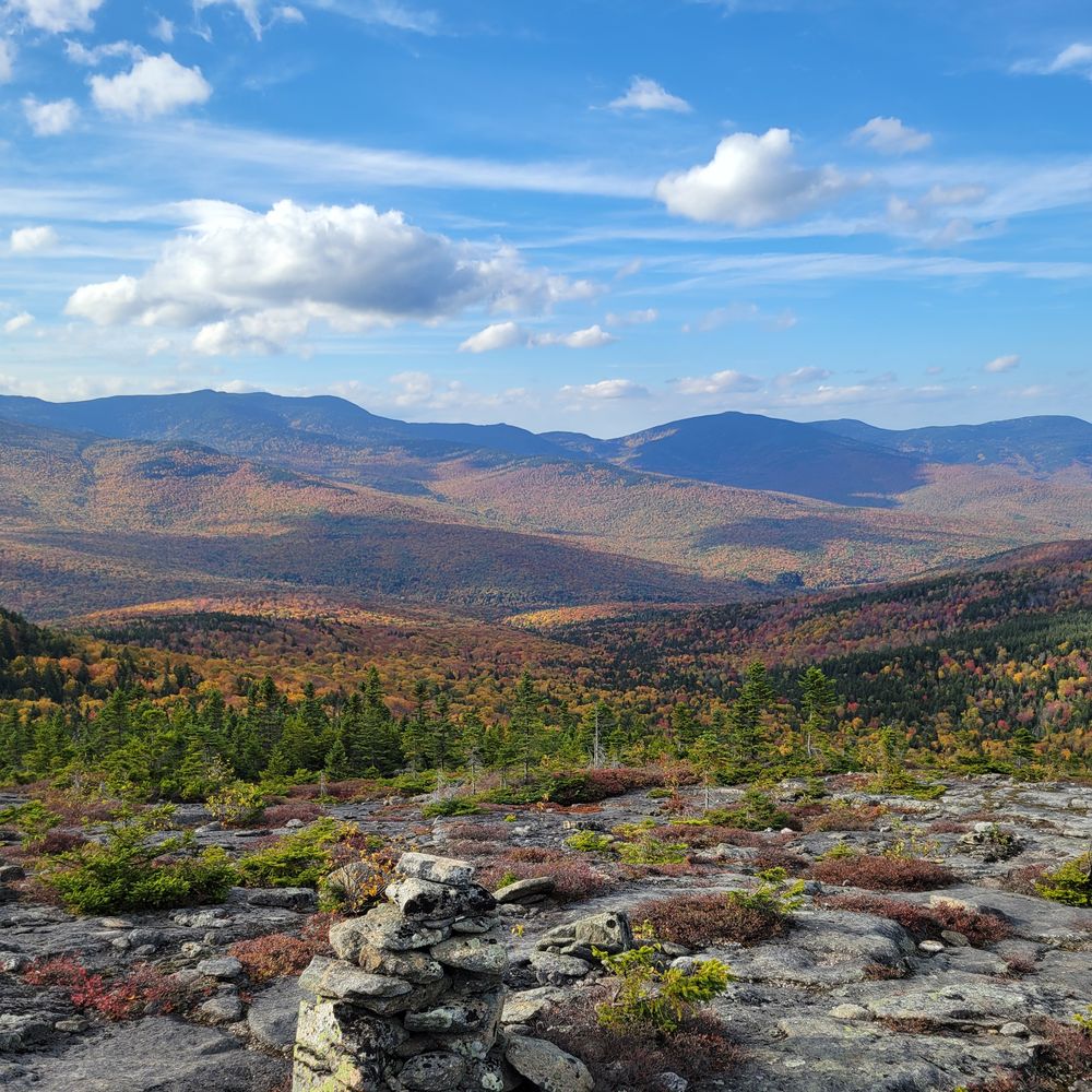 Fall foliage across rolling mountains, seen from an alpine ledge